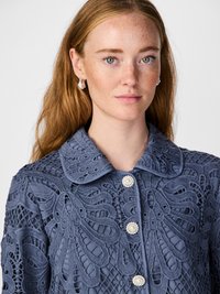 Blue embroidered jacket featuring a floral lace design, large collar, and pearl buttons. Textured fabric with intricate detailing.