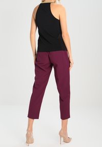 Svart ärmlös topp med racerback-design, matchad med burgundy förkortade byxor och nude högklackade skor. Slät tyg med avslappnad passform.