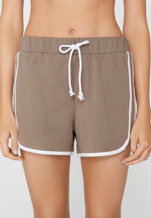 Frau trägt braune Freizeit-Shorts mit weißem Saum und weißem, gebundenem Kordelzug an der Taille, die den Mittelteil und die oberen Beine zeigen.