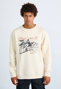 Sudadera color crema hecha de una tela suave, con un diseño gráfico de esquí que presenta contornos en negro y acentos en tonos pastel. Cuello redondo y mangas largas.