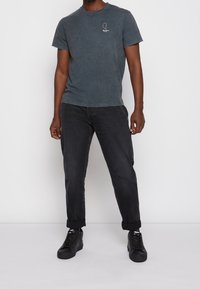 Šedé bavlněné tričko s malým bílým logem na hrudi, spojené s černými rovnými džínami a černými teniskami.