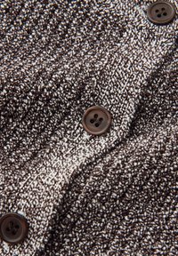 Close-up van bruin-wit gebreide stof met drie donkerbruine knopen met vier gaten, in een verticale lijn genaaid.