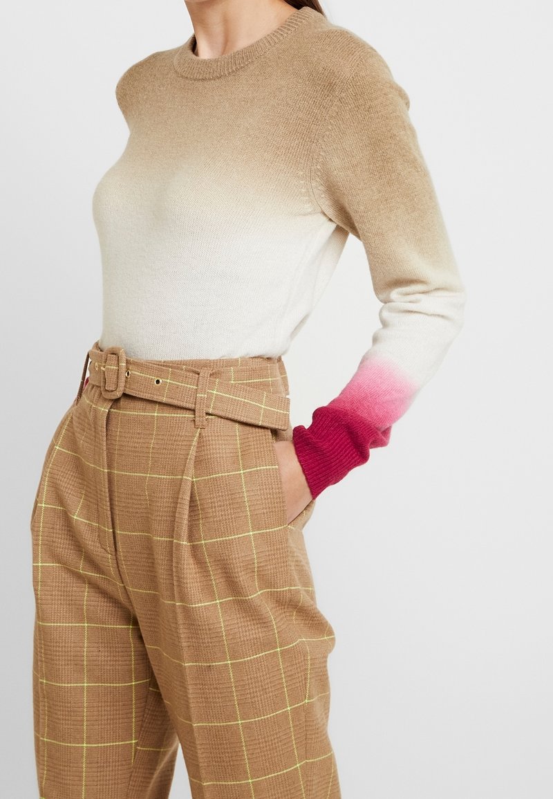 Beige och krämfärgad gradienttröja med rosa detaljer, rundhalsad och ribbade ärmmuddar, tillsammans med bruna rutiga högmidjade byxor med bälte.