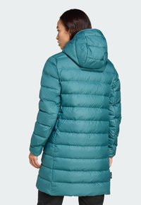 Teal zimska jakna s kapuljačom, s karakterističnim kočenim dizajnom i dužim krojem. Glatka tekstura s vidljivim šavovima i detaljem oznake sa strane.