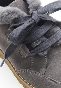 Zapato de ante gris con un suave collar de piel sintética gris, cordones planos trenzados y una suela de goma texturizada con una costura.