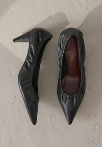 Schwarze Lederhighheels mit spitzem Zehenbereich, geraffter Textur rund um die Öffnung und glatter Innenauskleidung.