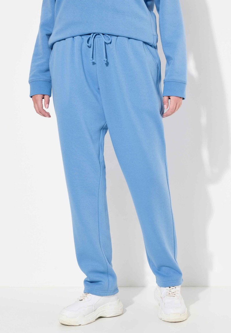 Pantalones deportivos de color azul claro, hechos de una tela suave, con una cinturilla elástica y cordón ajustable, además de bolsillos laterales. Combinados con zapatillas blancas.