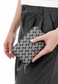 Gray geometric-patterned wallet made of textured material, featuring a zip closure and silver hardware, held in a hand near a dark garment.