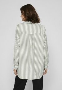 Camisa de manga larga a rayas en verde claro y blanco, con un cuello abotonado, pliegue en la espalda y dobladillo redondeado, y puños abotonados.