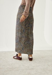 Larga falda estampada en azul oscuro con diseños de hojas en verde, marrón y dorado. Combinada con zapatos burdeos con acentos en blanco.