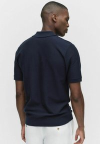 Mörkblå kortärmad polo med ribbad krage och manschetter, med en strukturerad stickning och en figurnära design vid midjan.