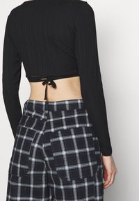 Top corto nero a costine con maniche lunghe, caratterizzato da un dettaglio sul retro con lacci. Abbinato a pantaloni cargo a quadri blu e bianchi con tasche laterali.
