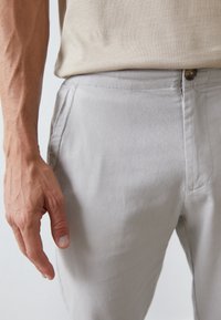 Light gray pants made of soft fabric, featuring a straight fit, side pockets, and a button closure at the waistband.