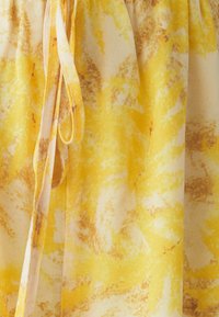 Geltonos spalvos audinys su marmuro raštu, kuriame dera šviesesnės ir tamsesnės geltonos bei rudos spalvos atspalviai. Yra liemens raištelio detalė, leidžianti reguliuoti apimtį.