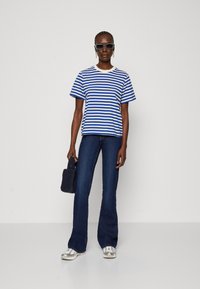 Blå og hvid stribet t-shirt med rund hals, parret med mørke flared jeans og sølv sneakers. Sort tekstureret håndtaske og solbriller.