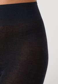 Svarta strumpbyxor med en texturerad midjeband, med ett ribbat mönster. Materialet verkar vara stretchigt och åtsittande, designat för komfort.