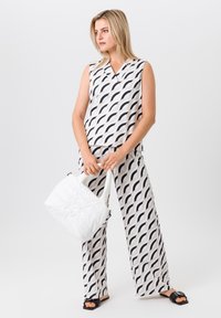 Top sans manches et pantalon large dans une couleur crème avec un motif de vagues bleu marine. Complété par un sac matelassé blanc et des sandales noires.