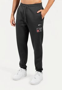 Schwarze Jogginghose mit elastischem Bund, Seitentaschen und einem Aufnäher mit der Zahl "01". Sie hat eine glatte Textur und eine lockere Passform.