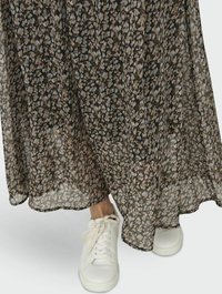 Abito nero fluente con un motivo floreale in colori tenui, abbinato a sneakers bianche basse. Il tessuto è trasparente e leggero.