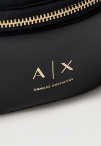 Λεπτομέρεια μαύρης τσάντας Armani Exchange με χρυστό φερμουάρ και χρυσό ανάγλυφο λογότυπο A|X σε λεία επιφάνεια.