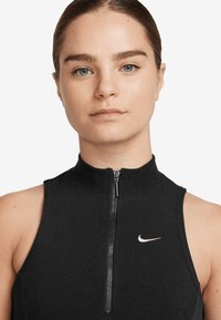 Top preto sem mangas com colarinho alto e fecho na frente. Apresenta uma textura canelada e um pequeno logo branco da Nike no peito.