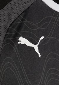 Juodas sportinis audinys su tekstūriniu raštu ir ryškiu baltu Puma logotipu. Dizaino akcentai - subtilios bangos linijos tamsesnėse atspalviuose.
