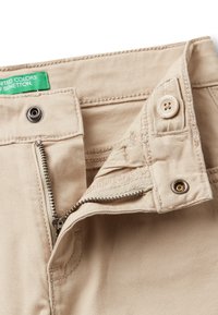 Pantalones de algodón beige con cremallera, cierre de botón, acentos bordados y una etiqueta verde con "United Colors of Benetton."