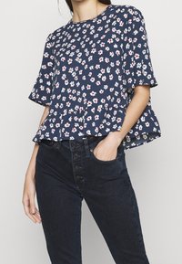 Navy blue floral peplum top featuring short sleeves, white and red flower patterns, and a round neckline, paired with dark denim pants.