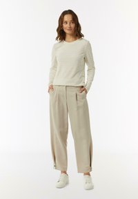 Langärmliges, cremegestreiftes Oberteil mit Rundhalsausschnitt, kombiniert mit hellbeigen, weiten Hosen mit seitlichen Taschen und Knopfdetails.