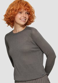 Haut gris à manches longues avec une texture lisse et légèrement scintillante, col rond et manches raglan. Remarquable par son design simple et minimaliste.