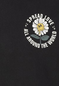 T-shirt nera con una grafica di un fiore bianco raffigurante un volto sorridente giallo e la scritta "Diffondi Amore in Tutto il Mondo."