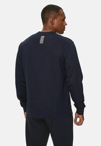 Felpa blu navy con maniche lunghe, collo a giro e vestibilità dritta. Presenta un design sul retro con strisce orizzontali bianche vicino al collo.