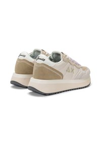 Sneaker beige con materiali in suede e mesh, suola spessa, lacci viola e un marchio distintivo sul tallone.