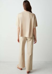 Top beige, morbido e largo con maniche corte, realizzato in tessuto liscio; abbinato a pantaloni beige chiaro a gamba larga e zoccoli in legno.