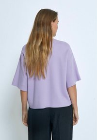 Top a maniche corte in maglia lavanda con vestibilità rilassata, presenta un colletto rotondo e orlo dritto. Indossato con pantaloni neri a gamba larga.