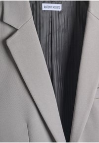 Blazer gris con solapas estructuradas, que presenta un exterior texturizado y un forro a rayas negras. La etiqueta dice "ANTONY MORATO."
