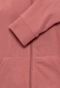 Felpa rosa con zip, dal tessuto morbido, con tasche frontali e cuciture a contrasto sui polsini e sulla cerniera. Vestibilità rilassata.