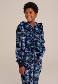 Zila kamuflāžas polāra kombinezons ar rāvējslēdzēju priekšpusē, kapuci un ribotām aprocēm. Izceļas ar mīkstu tekstūru un dažādām zilās un tumši zilās krāsas tonalitātēm.