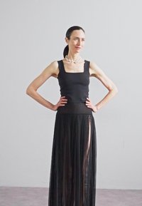 Μαύρο αμάνικο μπλουζάκι συνδυασμένο με μια μακριά, διάφανη μαύρη πλισέ φούστα. Η φούστα διαθέτει υψηλό σκίσιμο και ζώνη με διακριτή υφή.