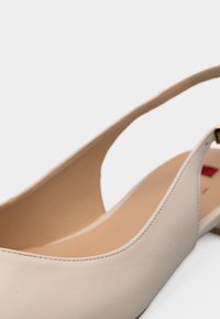 Γυναικείο μπεζ παπούτσι slingback με χαμηλό τακούνι, επάνω μέρος από λείο δέρμα και ανοιχτό καφέ εσωτερική σόλα, ορατό πάνω σε λευκό φόντο.