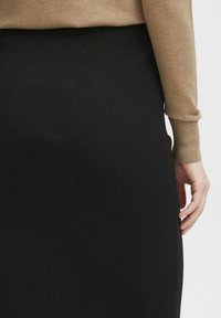 Der schwarze gerippte Strickrock hat einen hohen Taillenbund und eine vertikale Textur und wird mit einem figurbetonten taupefarbenen Pullover kombiniert. Nahaufnahme auf der Taille.