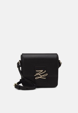 Borsa a tracolla in pelle nera con chiusura a patta, caratterizzata da un logo in tono oro e una tracolla regolabile. Texture liscia, forma rettangolare.