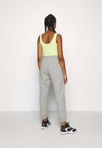 Grijze joggers met elastische boorden, gecombineerd met een felgroene tanktop met een geschulpte halslijn. Zwarte sportschoenen maken de outfit compleet.