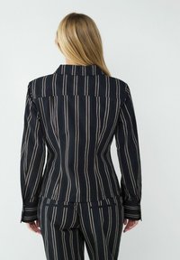 Gestreifter Blazer in Schwarz mit vertikalen Linien in Weiß und Beige. Taillierte Passform, lange Ärmel und klassischer Kragen. Glatte Stofftextur.