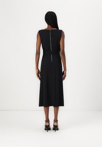 Robe noire sans manches avec un corsage ajusté et une jupe évasée à mi-mollet. Détail de fermeture éclair au dos et tissu lisse. Associée à des talons avec lanières.