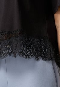 Top negru cu dantelă pe margine și motive florale, asortat cu un material de culoare bleu deschis dedesubt. Textură netedă și design lejer.