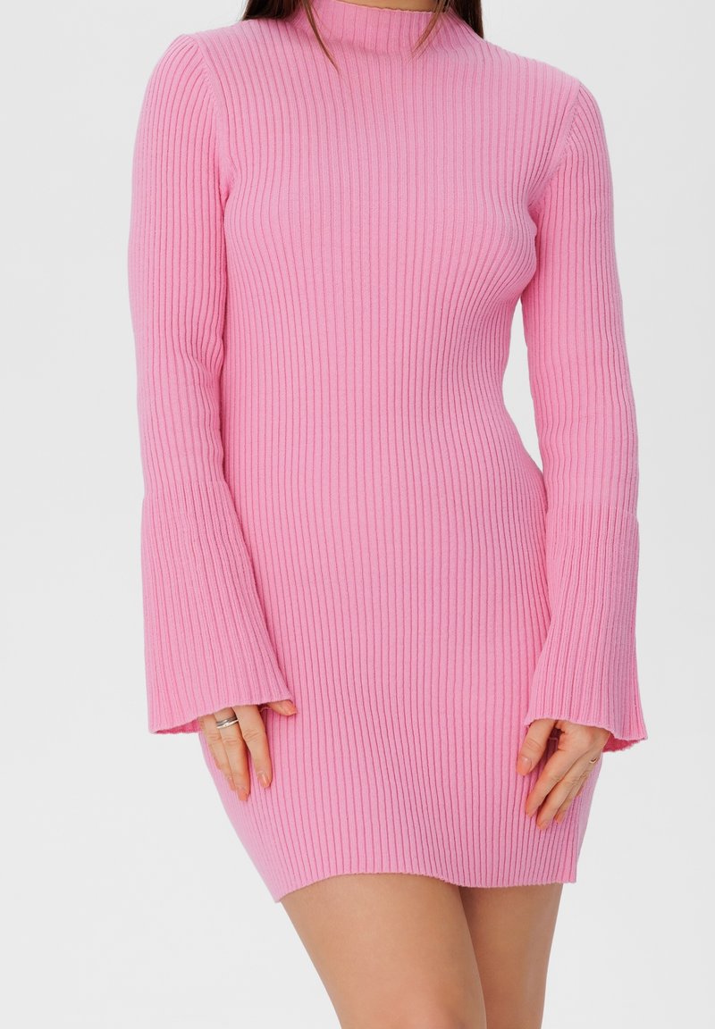 Mini-robe rose côtelée avec manches longues évasées et col montant, réalisée en matière douce en maille, présentant une coupe ajustée et un tissu texturé.