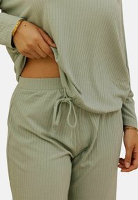 Ensemble de loungewear vert clair en côte, comprenant un haut à manches longues et un pantalon à taille élastique, avec un détail de cordon de serrage et une texture douce.