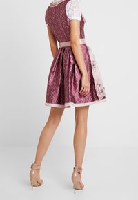 Robe bordeaux en tissu texturé, jupe plissée et accents brodés ; associée à des sandales à talons nus.