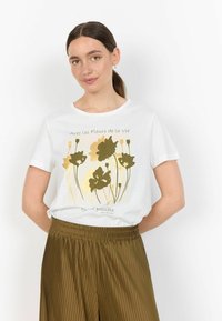 T-shirt bianca in cotone con una grafica floreale in tonalità oro e verde, maniche corte, scollo rotondo, abbinata a pantaloni plissettati color olive.